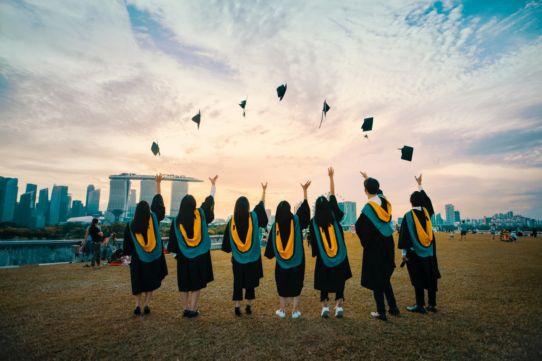 Students in graduation gowns tossing their caps outdoors with a city skyline in the distance; illustrative student photography.